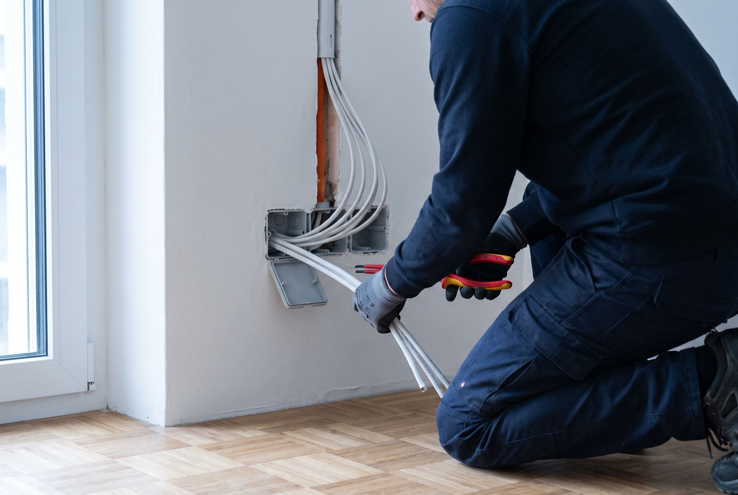 Elektriker zieht neue Leitungen in eine Unterputzdose in einer frisch verputzten Wand